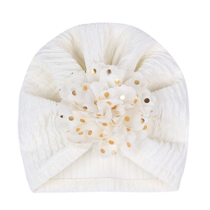 Detail of white newborn turban hat with ribbed texture and gold-dotted 3D flower