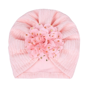 Pink knit baby turban hat with a large gold polka dot floral decoration on white background