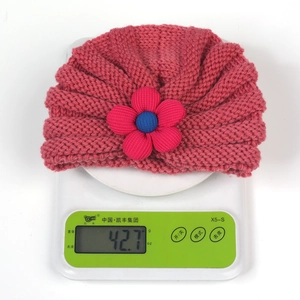 Detailed view showing a handmade pink knit baby hat with flower weighing 42.7g on scale