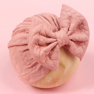 Close-up of baby beanie with diamond-patterned texture and a large soft bow detail