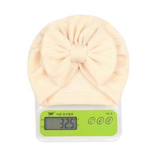 Détail du bonnet turban beige pour bébé avec nœud pesé sur une balance à 32,5g