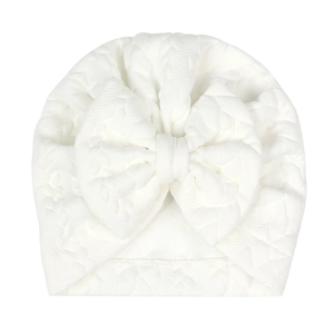 Close-up detail of white knitted baby hat featuring a large decorative bow on front