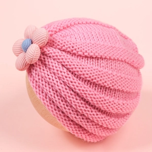 Detailed knit texture of light pink baby hat with 3D fabric flower on a wooden stand
