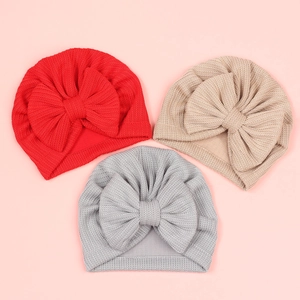 Gros plan de trois bonnets bébé en maille gaufrée avec nœuds en rouge, beige et gris