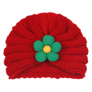 Detail of red knit baby hat featuring a 3D green flower decoration and ribbed texture