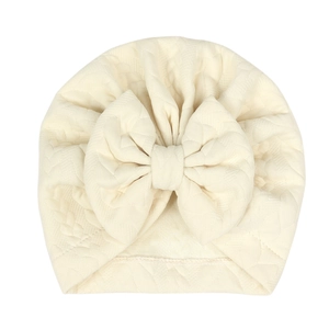 Close-up of quilted cream baby beanie with a large bow detail and soft cotton texture