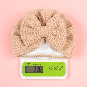 Macro detail of infant waffle knit bow hat in beige showing 33.8g weight on scale