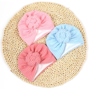 Détail de trois bonnets pour bébé en tissu côtelé rose et bleu sur un tapis tissé naturel