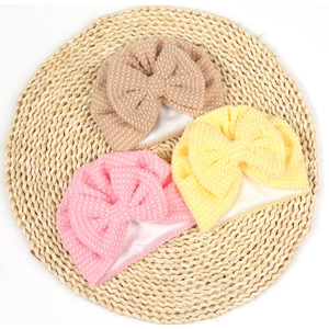 Detailed view of three soft bow baby hats in pink, yellow and brown on a woven mat