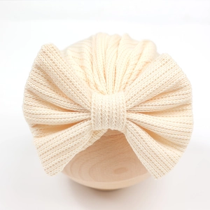 Détail du bandeau tricoté crème pour bébé avec un grand nœud sur support bois