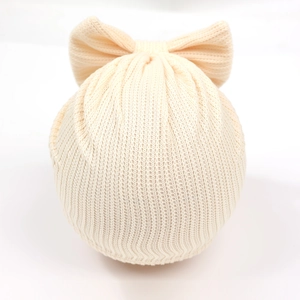 Détail d'un bonnet tricoté beige pour bébé avec un grand nœud sur un modèle en mousse