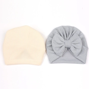 Détail de bonnets tricotés pour bébé beige et gris avec un grand nœud gaufré