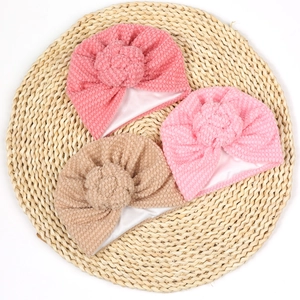 Détail de trois bonnets bébé à pois 3D et nœuds floraux sur un support en paille