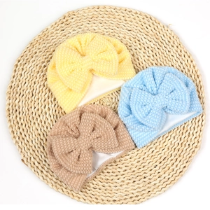 Close-up of three textured bow beanies for infants in yellow, blue and brown