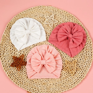 Detail of three infant turbans with bow in white and pink tones on woven mat
