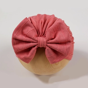 Close-up of coral pink newborn baby hat with ribbed knit texture and large bow detail
