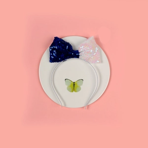 Dettaglio di un cerchietto con fiocco di paillettes blu e bianco su sfondo rosa