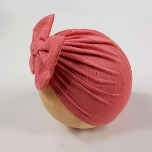 Detail of coral baby turban with diamond texture knit and large bow on a wooden head stand