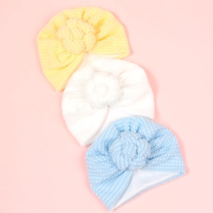 Détail de bonnets gaufrés pour bébé en jaune, blanc et bleu avec pompons à fleurs