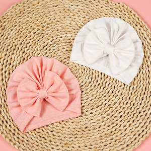 Close-up of baby turban hats with large bows in pink and white waffle knit fabric