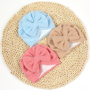 Close-up of three textured baby beanies with large bows in blue, pink, and beige colors