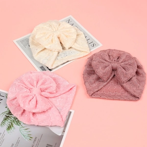 Détail de trois turbans tricotés pour bébé avec de grands nœuds en tons crème et rose