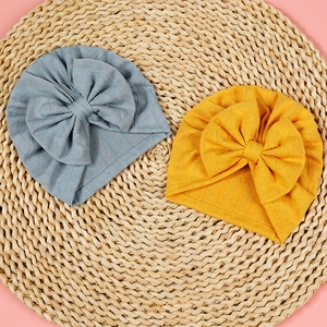 Detailed close-up of knitted baby hats with large bows on a straw mat background