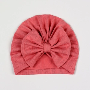 Detail of pink newborn baby hat featuring diamond knit texture and a large bow design