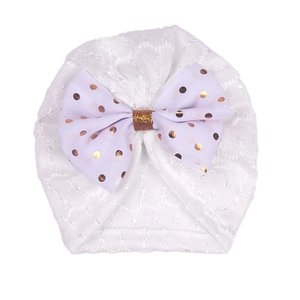 Détail du bonnet pour bébé en dentelle blanche orné d'un grand nœud à pois rose doré