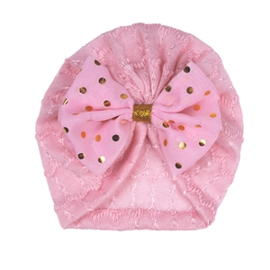 Détail du bonnet turban rose bébé avec nœud à pois dorés et texture dentelle ajourée