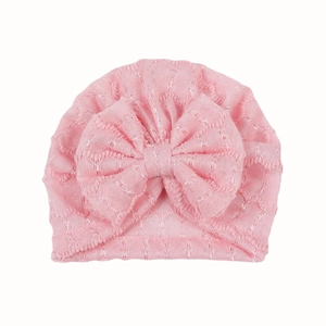 Détail du turban rose en tricot pour bébé avec texture évidée et décoration de nœud papillon