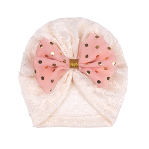 Détail du béguin pour bébé avec dentelle crème et grand nœud rose à pois dorés