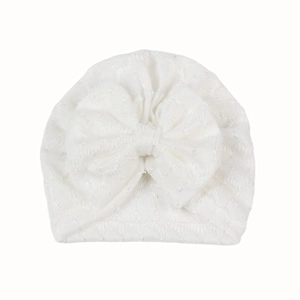 Détail du bonnet en tricot blanc pour bébé avec motifs dentelle et un grand nœud décoratif