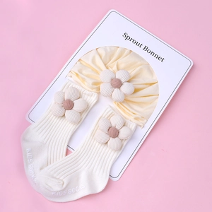 Detail of knitted baby turban and socks set with 3D floral accents on pink background