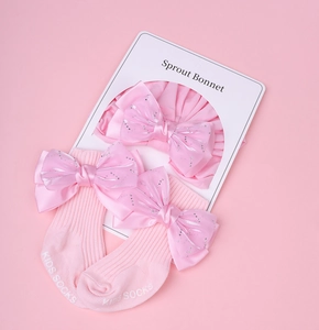 Détail de l'ensemble bonnet et chaussettes en coton rose avec nœud à paillettes