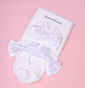 Détail de l'ensemble bandeau et chaussettes pour bébé avec nœud pailleté blanc sur fond rose