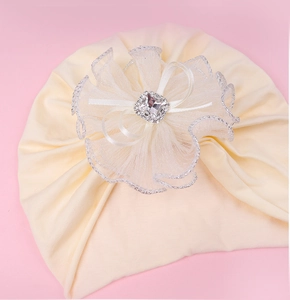 Détail de la grande fleur en dentelle avec strass carré sur bonnet turban pour bébé beige