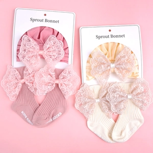 Close-up of pink and beige knitted baby bonnet and socks set with large lace bows