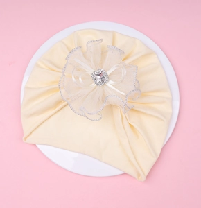 Gros plan du bonnet bébé crème avec une fleur en dentelle et un strass carré