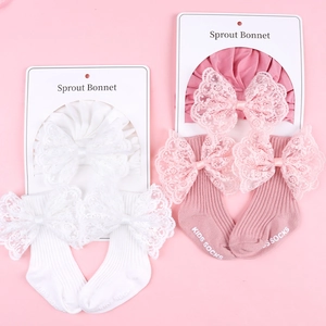Close-up of white and pink infant sets with lace bow hats and matching ribbed socks