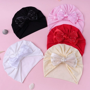 Détails de cinq turbans pour bébés avec grands nœuds en strass sur un fond rose doux