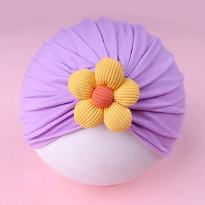 Detail of purple baby hat with a yellow 3D flower decoration and pleated cotton fabric