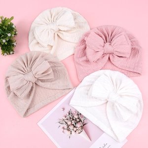 Détail de quatre bonnets bébé à nœud en tricot torsadé doux aux couleurs pastel