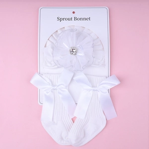 Detailed view of white baby lace flower hat and matching socks with satin bows