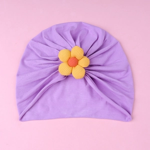 Detail view of baby turban hat in light purple featuring a vibrant yellow sunflower accent
