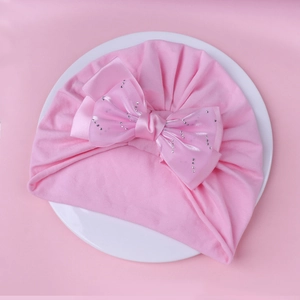 Détail du bonnet turban bébé en coton rose avec grand nœud en strass sur l'assiette