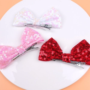 Close-up of three sparkling sequin hair bows in white, pink, and red with metal clips