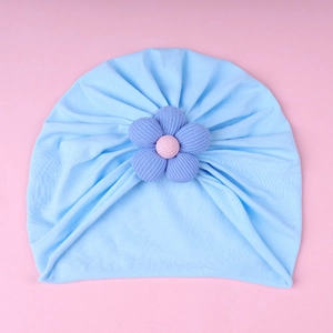 Close-up of sky blue baby turban hat with a purple knit flower on a pink background