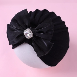 Détail d'un bonnet turban noir pour bébé avec un grand nœud et strass carrés brillants