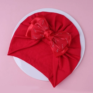 Détail du bonnet turban rouge pour bébé avec un grand nœud en strass sur une assiette